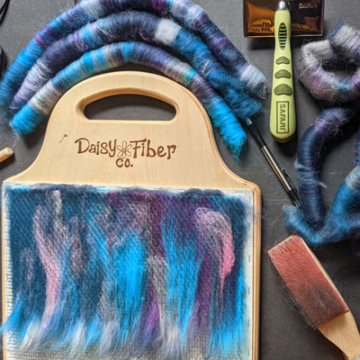 Colorful fibers in shades of blue and purple on a blending board