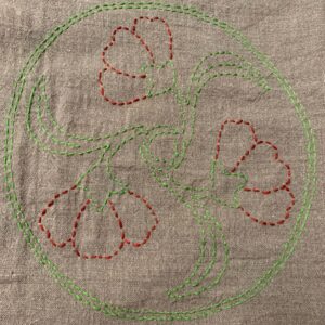 image of flowers outlined in red and green stitches on a tan fabric