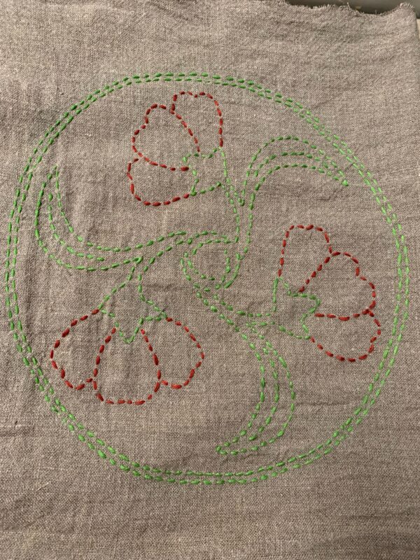 image of flowers outlined in red and green stitches on a tan fabric
