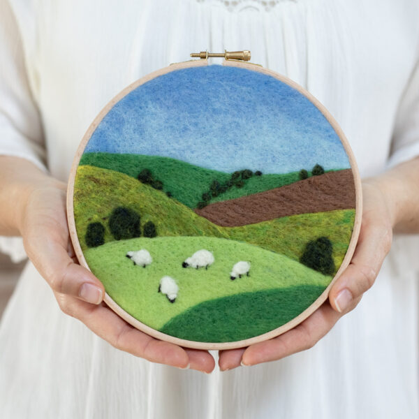 Needle felted landscape featuring sheep on rolling hills under a blue sky