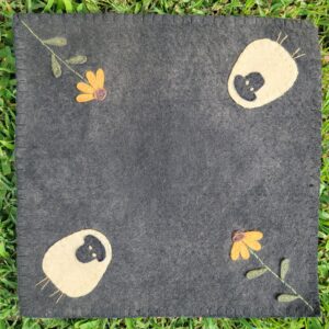 a square of gray felt with felted sheep and flowers embroidered into corners